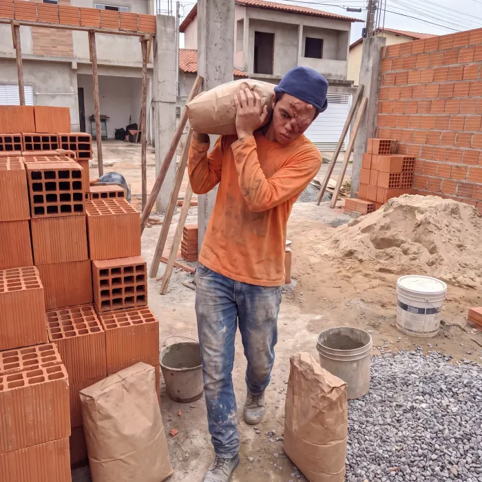 Trabalhador carregando um saco de cimento nas costas em um canteiro de obras